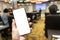 Hand holding the smartphone with blank screen on blurred image of people in conference room for meeting seminar as background.