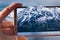 hand holding a smartphone taking a photo of a mountain landscape, a winter day