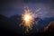 Hand holding a sparkler burning in outdoor setting, mountain landscape, at dusk