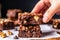 hand holding a square piece of brownie with crunchy walnuts on top