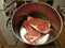Hand holding steak in metal pot in kitchen