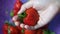 A hand holding a strawberry with blurry strawberry background on the basket