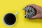 Hand holding striped donut coffee yellow background