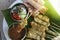 Hand holding Thai pork satay with peanut sauce, cucumber salad and grill bread in white plate.