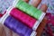 Hand holding three colorful spools of thread in purple, pink and green