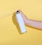 hand holding a tin can and spraying a product over yellow background