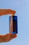 Hand holding transparent glass perfume bottle. travel size vial against blue sky