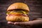 Hand holding vegetarian craft burger with cheese, orange, basil leafs, shiitake mushroom and purple onion on wood table and rustic