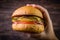 Hand holding vegetarian craft burger with cheese, orange, basil leafs, shiitake mushroom and purple onion on wood table and rustic