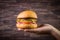 Hand holding vegetarian craft burger with cheese, orange, basil leafs, shiitake mushroom and purple onion on wood table and rustic