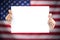 Hand holding white blank paper sheet mockup with US flag blurred