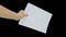 A hand holding a white empty piece of paper A4 with copy space against black background