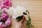 Hand holding white peony flower on background of peony bouquet on wood