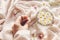 Hand holding white wildflower on background of soft beige fabric with glass cup with daisy flowers and jewelry in sunny light.