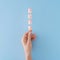 Hand holding the wooden stick with pastel sweets on a pastel blue background. Minimal flat lay