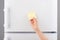 Hand holding yellow sticky paper note on white refrigerator