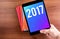 Hand holdling tablet with 2017 year number on screen over notebook on wood table,Digital happy new year card, Leave space for add