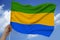 Hand holds against the background of the sky with clouds the color flag of Gabon on the texture of the fabric, silk with waves,