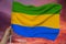 Hand holds against the background of the sky with clouds the color flag of Gabon on the texture of the fabric, silk with waves,