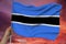 Hand holds against the background of the sky with clouds the colored flag of Botswana on the texture of the fabric, silk with