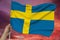 Hand holds against the background of the sky with clouds the colored flag of Sweden on a luxurious texture of satin, silk with