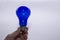 A hand holds a blue light bulb on a white background