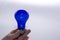 A hand holds a blue light bulb on a white background
