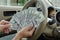 Hand holds cash dollars on the background of the steering wheel of a car. Concept of car sale, purchase and leasing.