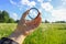 Hand holds a circular polarizer filter on field background.