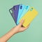 Hand holds the colored covers cases for the phone black, blue, yellow on the green background