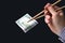 Hand holds dollars with bamboo chopsticks on a dark background. financial industry in food. cash spending concept