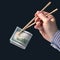 Hand holds dollars with bamboo chopsticks on a dark background. financial industry in food. cash spending concept