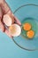 Hand holds an empty eggshell against the background of a cup with two yolks on a blue background. Step by step omelette