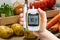 Hand holds glucometer for measuring glucose level. Vegetables in background.