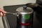 Hand holds handle of stainless steel pot on induction stove