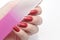 Hand holds nail file with red manicure on white background