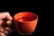 Hand holds orange mug with rosehip tea close-up on black isolated background. The health drink is recommended by traditional