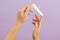 Hand holds plastic cream battle isolated on lilac background. Beauty concept. Packaging tube for cosmetic products