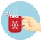Hand holds red cup with steaming cocoa. Hot chocolate drink with marshmallows and Christmas stick.