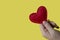 The hand holds a red heart made of fabric with white threads on a yellow background. Love, romance concept. Felt bright hearts wit