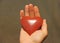 The hand holds a red or terracotta heart made of natural stone.