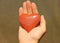 The hand holds a red or terracotta heart made of natural stone