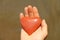 The hand holds a red or terracotta heart made of natural stone. Heart in hand. A stone in the shape of a heart. Love talisman, zen