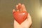 The hand holds a red or terracotta heart made of natural stone. Heart in hand. A stone in the shape of a heart. Love talisman, zen