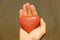 The hand holds a red or terracotta heart made of natural stone. Heart in hand. A stone in the shape of a heart. Love talisman, zen