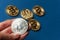 The hand holds a silver coin bitcoin on a blue background. The concept of crypto currencies