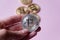 The hand holds a silver coin bitcoin on a pinkbackground. In the background there are several gold coins bitcoin.