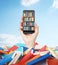 A hand holds a smartphone with a book shelf on the screen. A heap of colourful books. A concept of education and technology.Cloudy