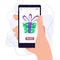 Hand holds a smartphone, while sending a gift. Online shopping gifts. Screen with present