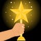 The hand holds the sports cup in the form of a golden star. Sports Cup gold stars in the hand of man on a black background.